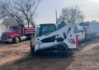 A close-up of a Bobcat E32 excavator with a black cab and white arm, set against a cloudy sky and industrial background.